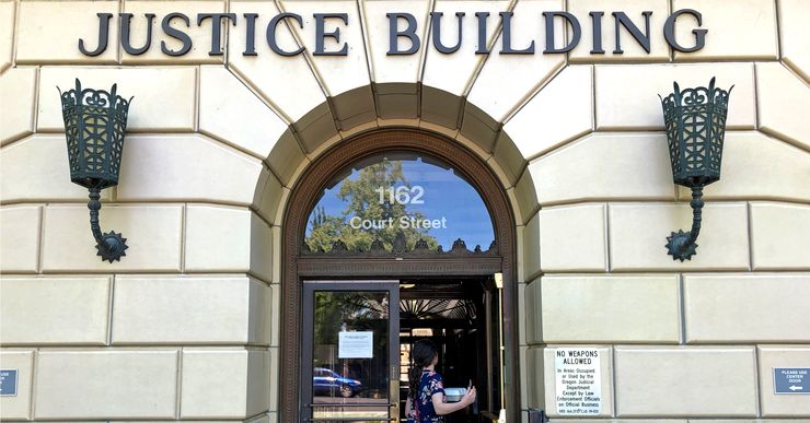 A woman enters a tan bricked building, with the signage "justice building" above the door. 