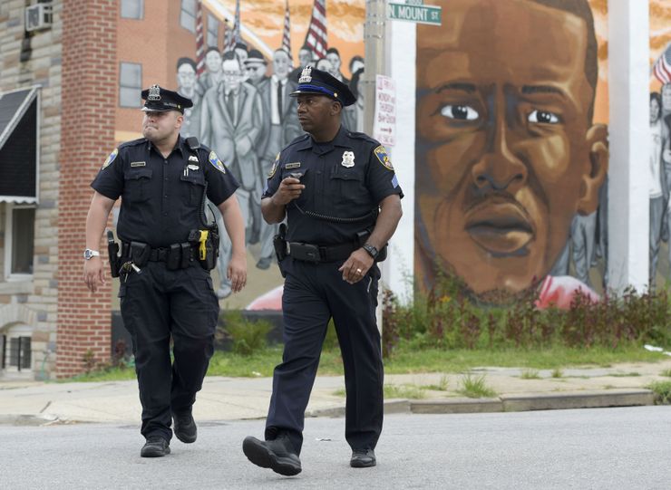 Baltimore police walk near a mural depicting Freddie Gray.