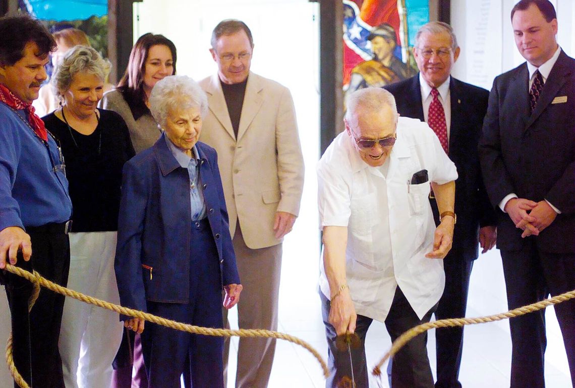 Charles Pearce uses a sword to cut the ribbon (rope) for the Pearce Civil War Collection and Western Art Gallery as his wife Peggy and others look on.