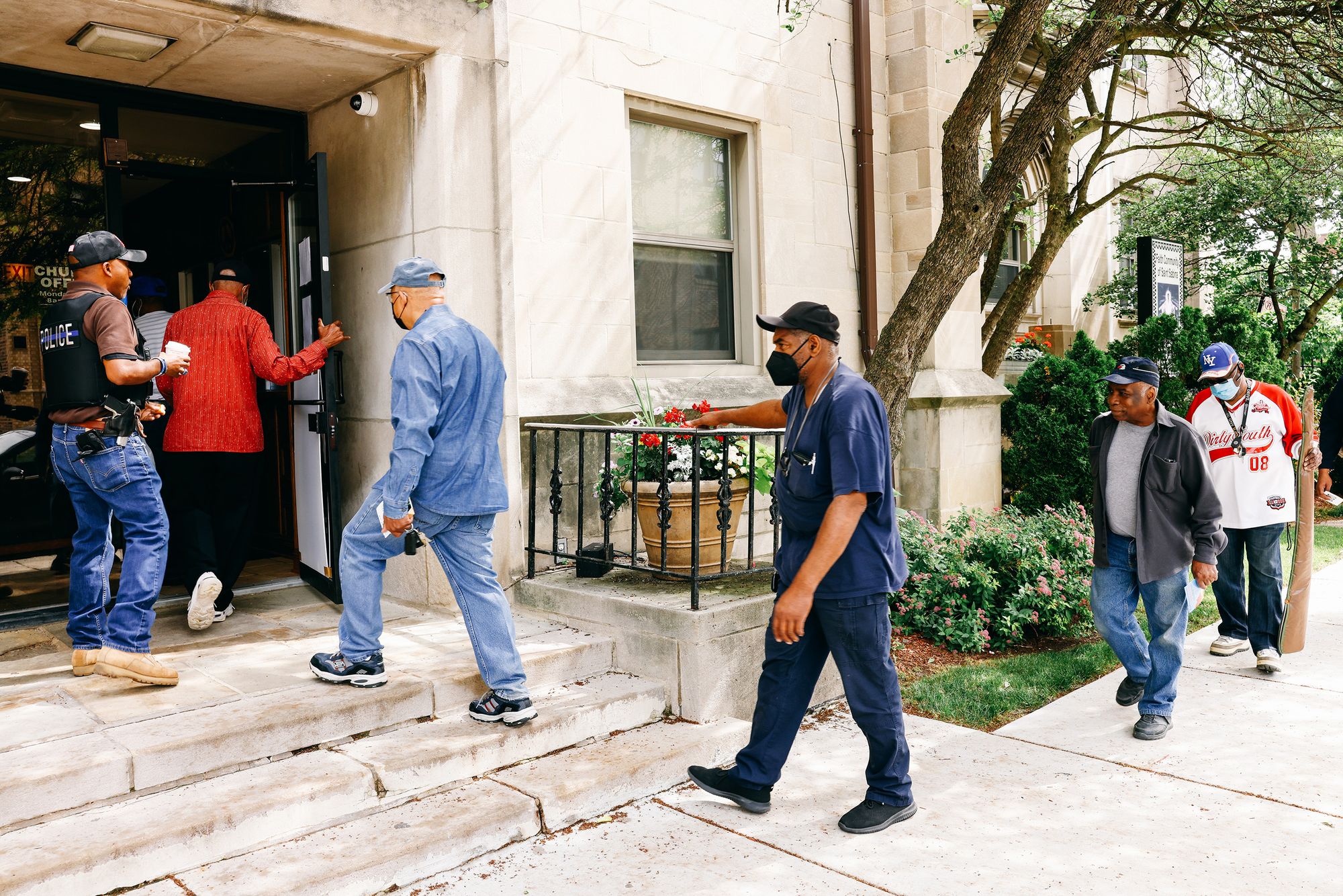 A line of individuals walk into a building. An officer stands at the entrance.