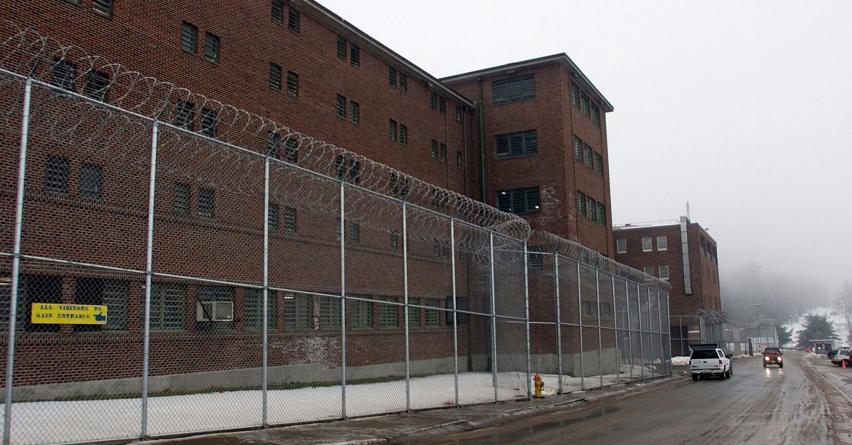 A red brick correctional facility behind a barbed wire fence. 