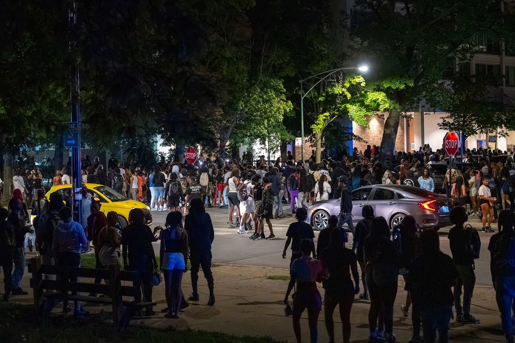 A photo shows a crowd of people outside walking in a street at night. 