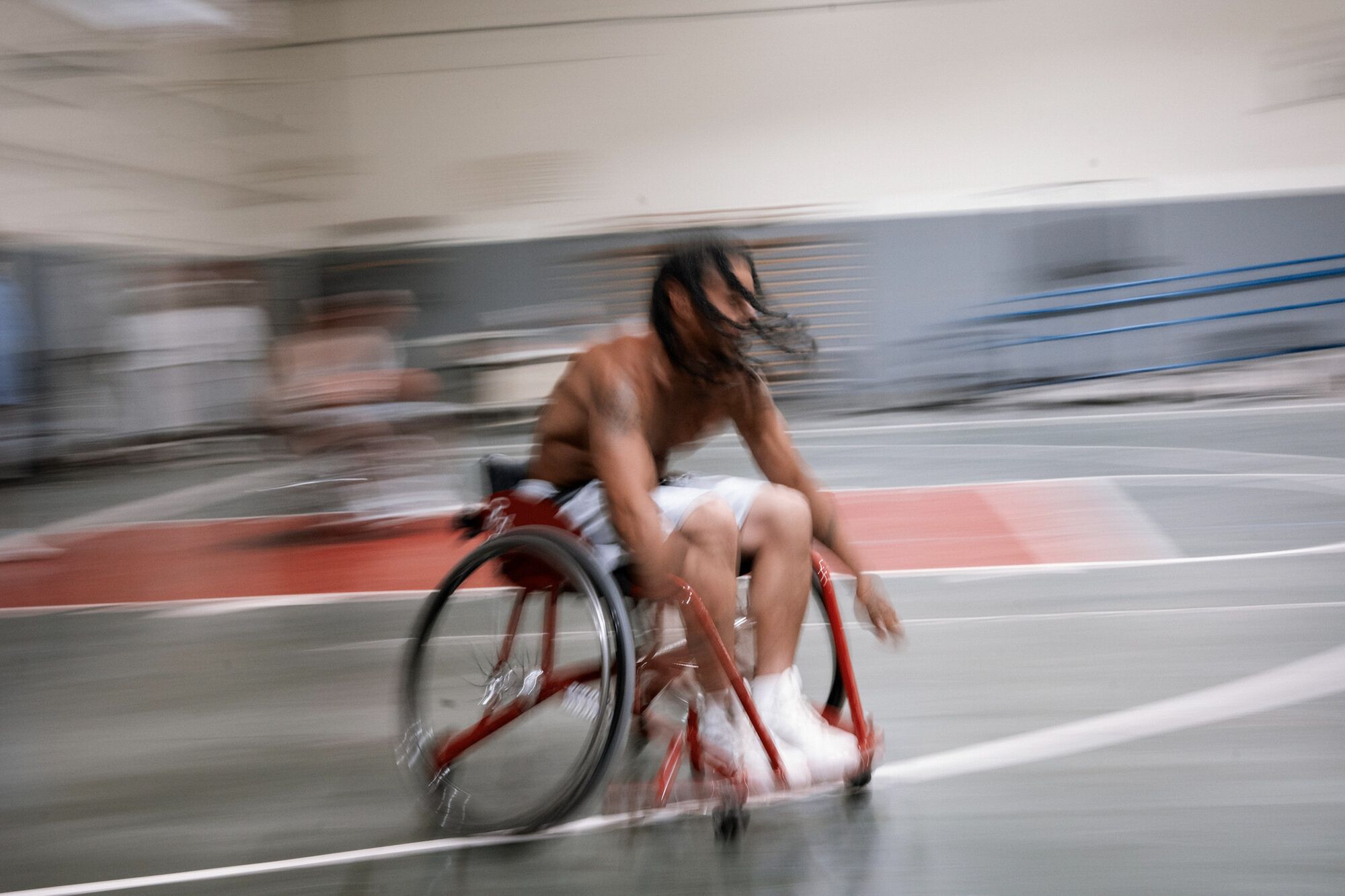 A photo shows a Black man with long hair speeding across the court in a blur in a wheelchair.
