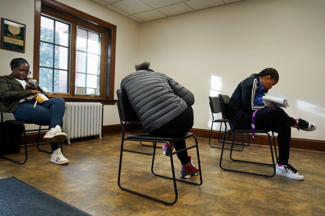 Three Black people sit in chairs waiting for their cases to be heard. 