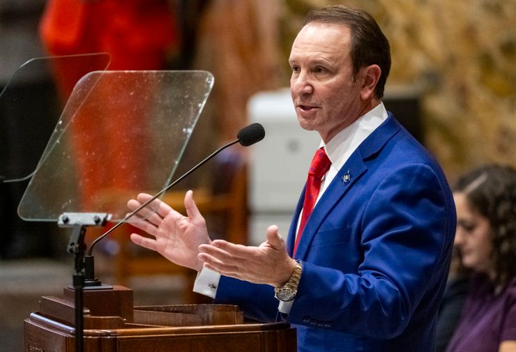 Gov. Jeff Landry, a White man wearing a blue suit and red tie, speaking at a podium in January 2024.  