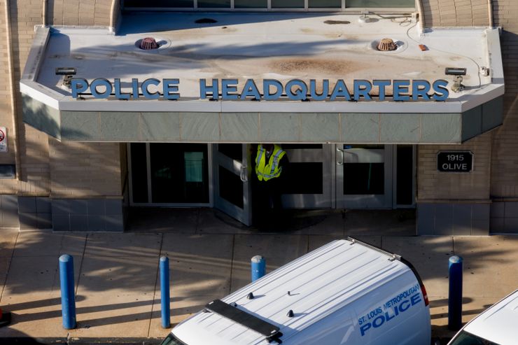 A view from above the awning of the St. Louis Police Department headquarters' entrance, where a man is standing in front of the metal doors. The man’s face is not visible.  
