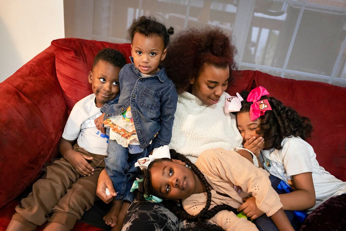 A Black woman sits on a red couch with her four children, posing for a portrait shot.