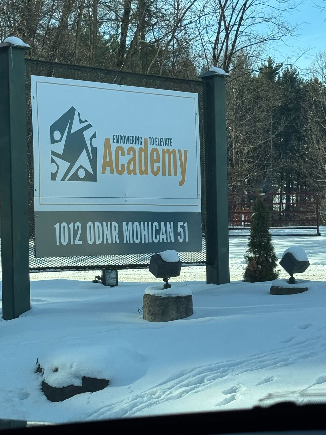 A photo shows a white, green and yellow sign with the words "Empowering to Elevate Academy" and the facility’s street address. 