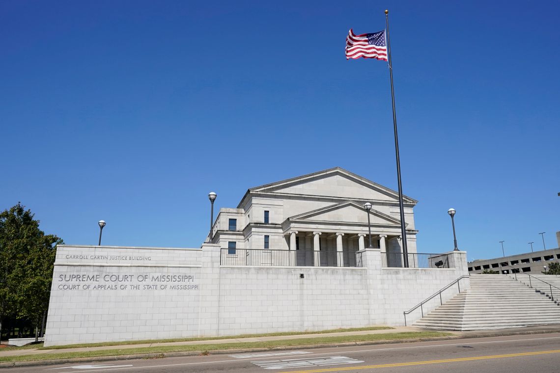 A white stone building with columns and pediments has steps leading up to it. The side of the building has block lettering stating “Supreme Court of Mississippi” and “Court of Appeals of the State of Mississippi.” There is a blue sky behind the building.