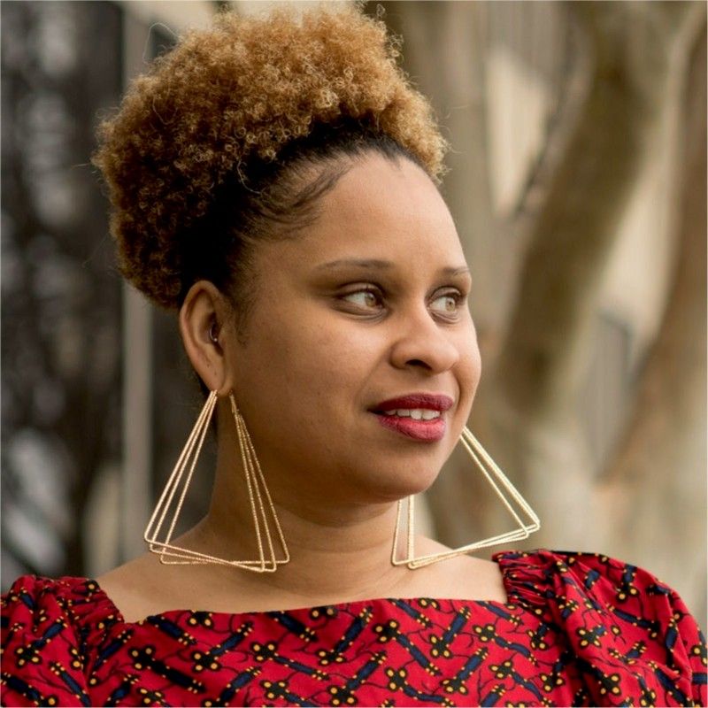 A portrait of Dacrie Brooks, wearing a red patterned shirt and triangle earrings.