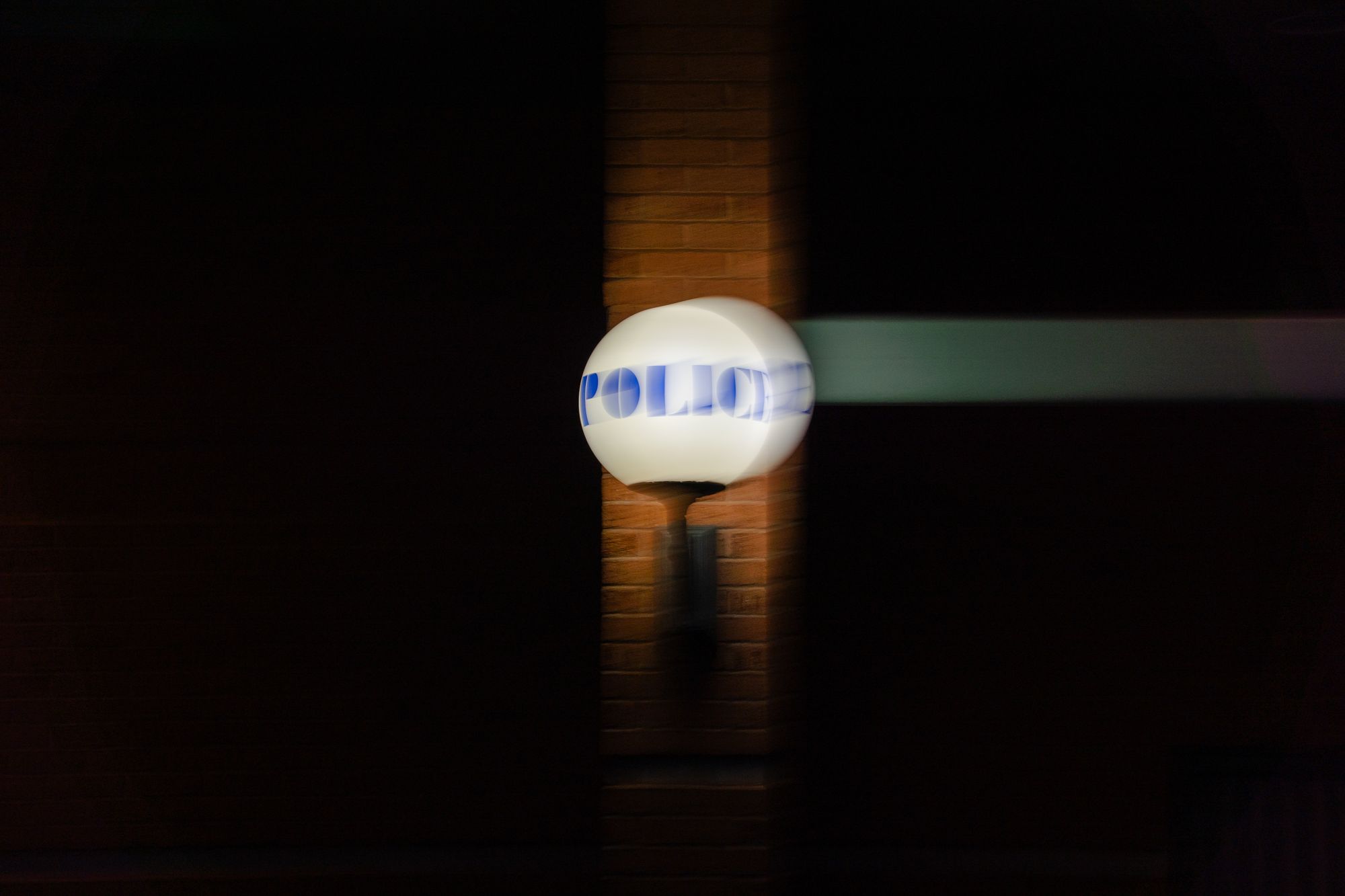 A round white light with the word "Police" on it is illuminated and blurred at the Stoughton Police Department headquarters.
