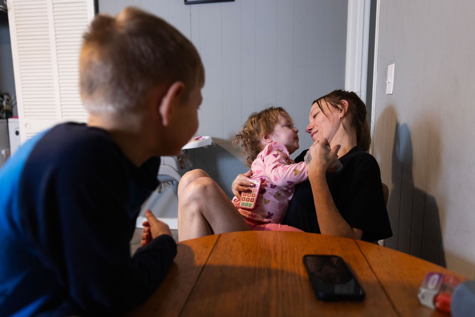 A photo of a White woman looking at her 2-year-old daughter while her son watches.
