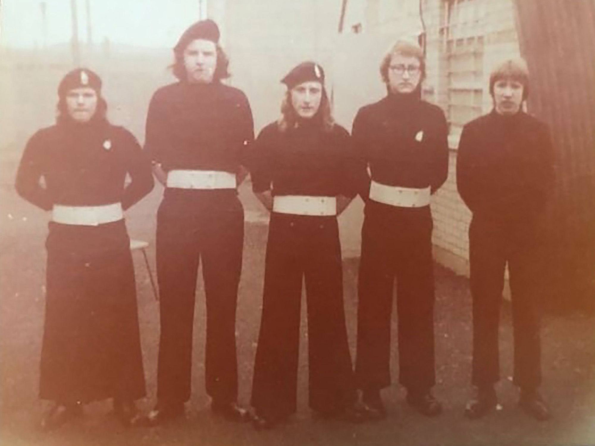 A sepia-toned photo shows a group of young adults wearing black and white uniforms while standing in one line. 