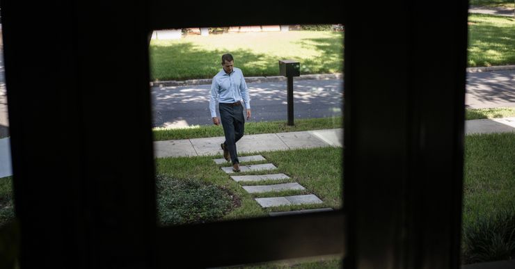 A White man wearing a blue-collared shirt and dark blue pants walks up a pathway.  