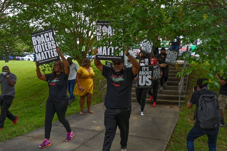 A color photograph of a group of Black people marching while holding signs that read “Black Voters Matter.” 