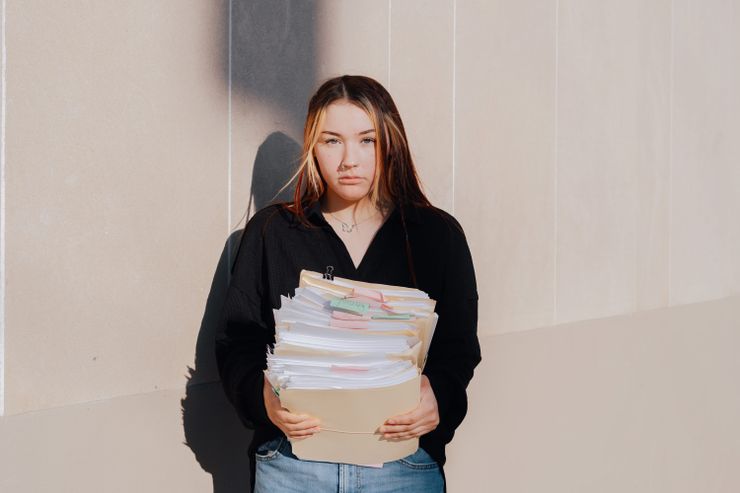 A photo shows a White woman with long brown hair and blonde highlights holding a stack of her paper records in manila folders. 