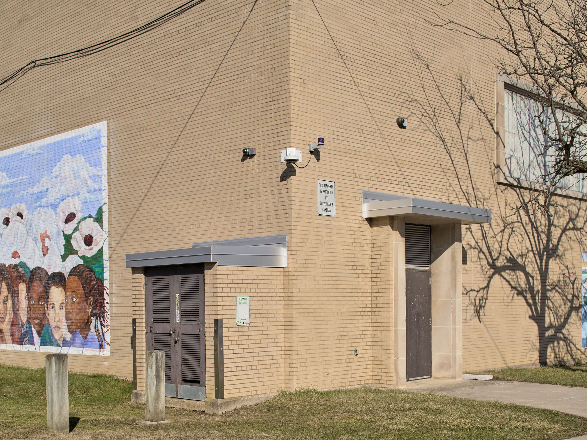 A photograph of a surveillance camera mounted on a recreation center with tan brick and a painted mural on the side. 