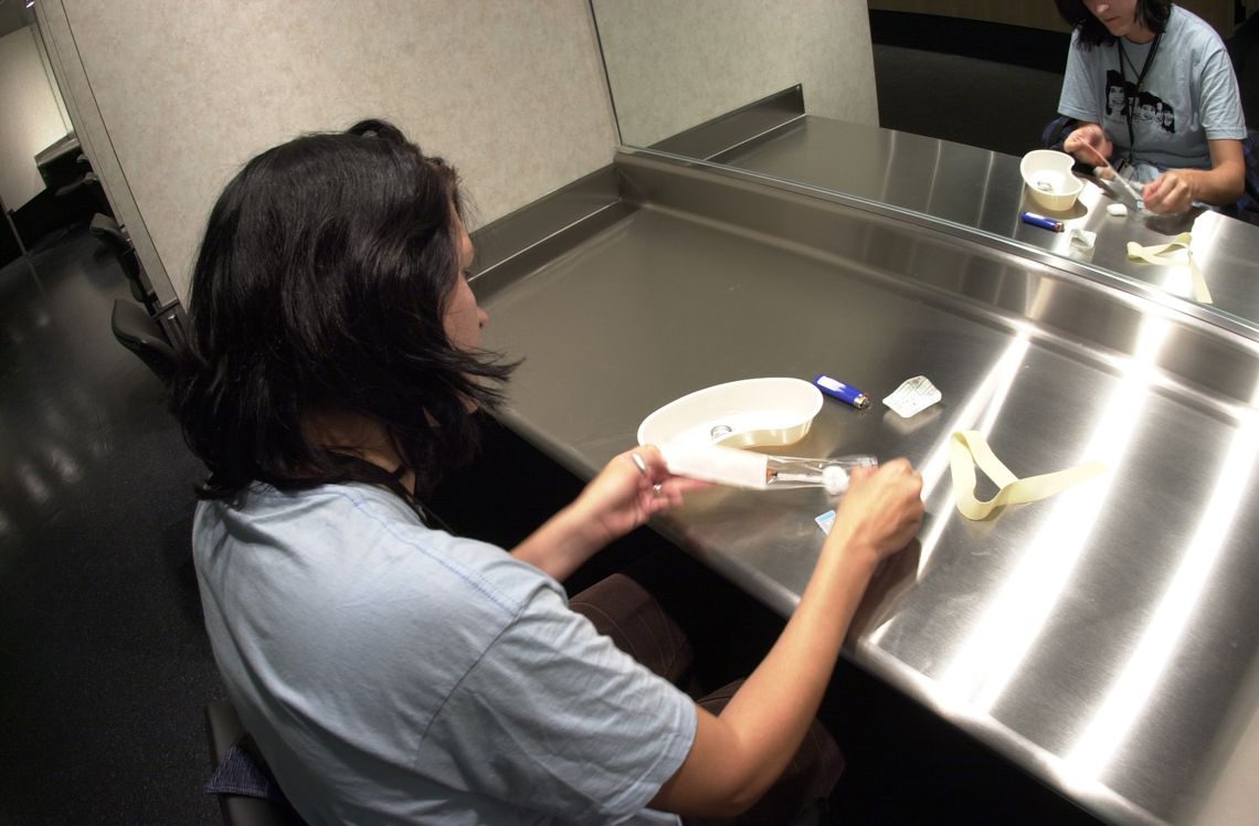 An peer counselor at Insite demonstrates how someone would use one of their injection booths. 