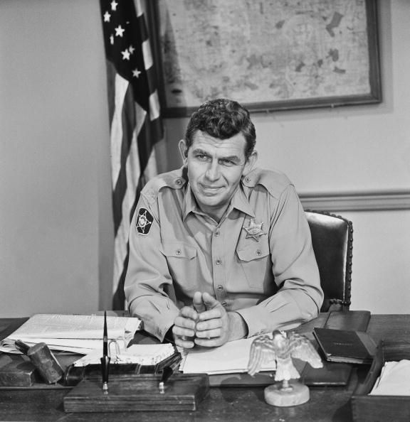 Andy Griffith, a White man with short dark brown hair and wearing a sheriff's uniform, playing Andy Taylor on "The Andy Griffith Show".