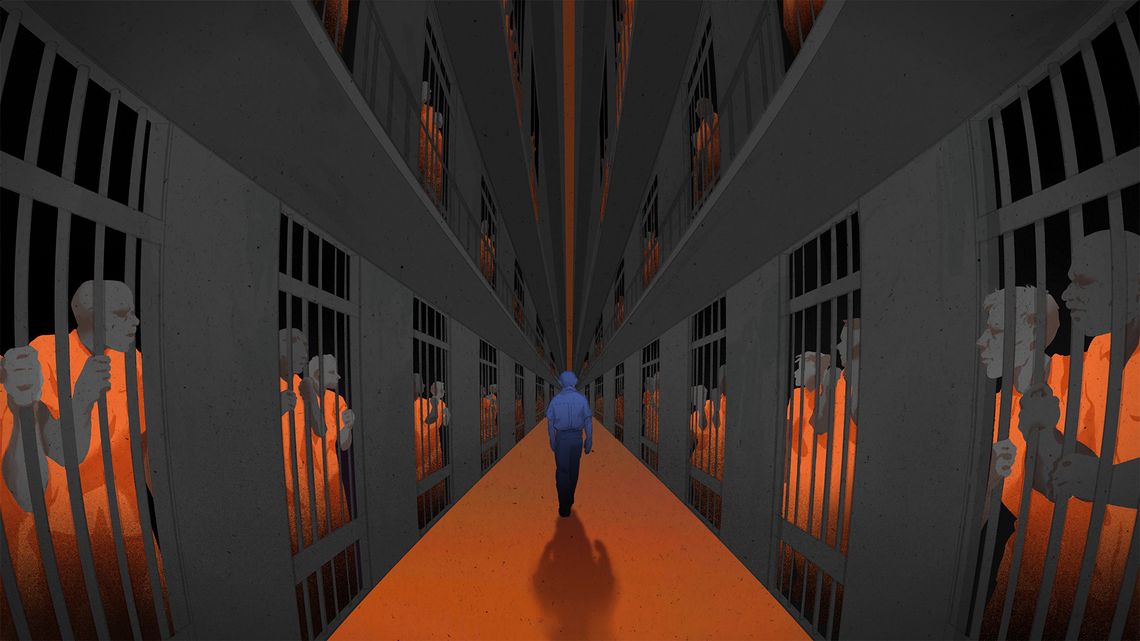 A lone correctional officer walking in a prison cell block while incarcerated people are confined in their cells. 