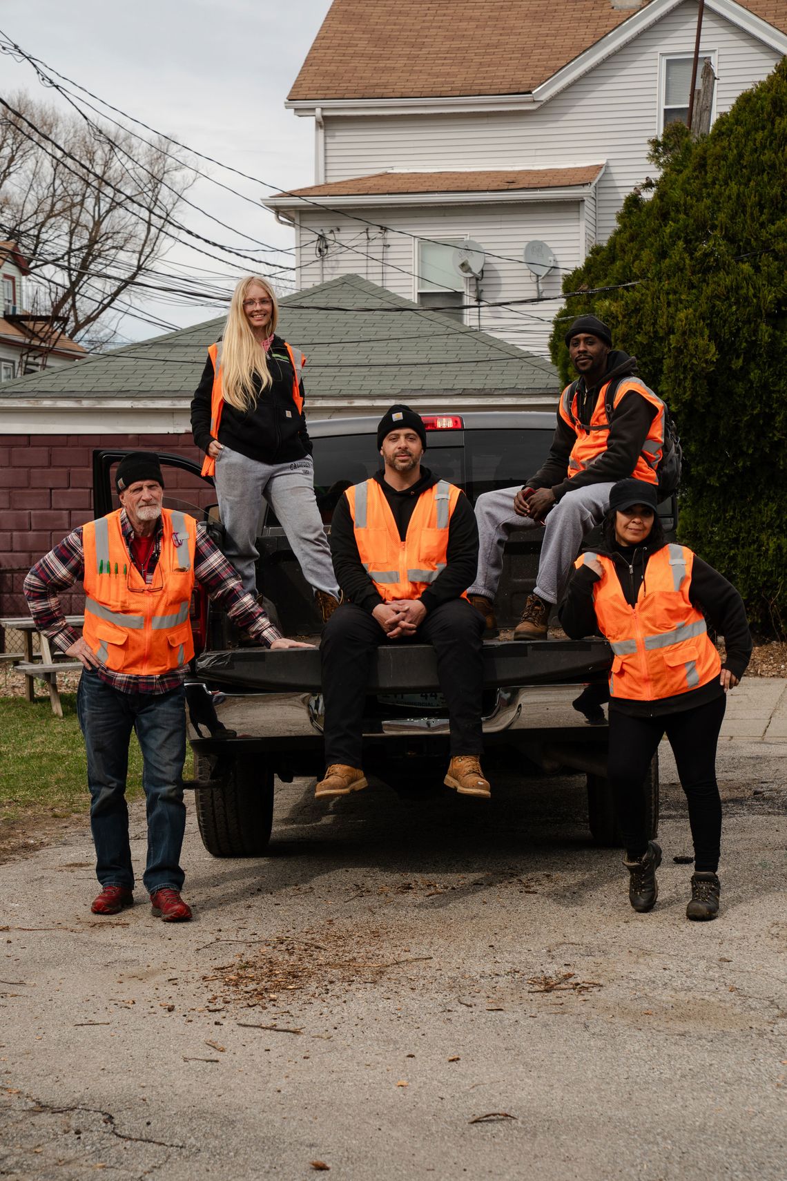 A photo of five people in orange safety vests sitting on and around a pickup truck while posing and looking into the camera. 