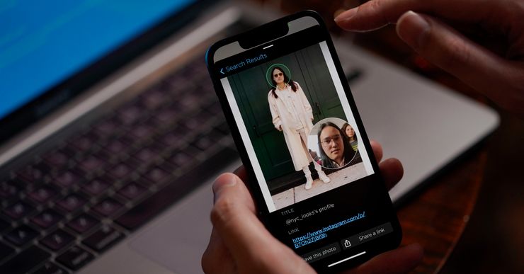 A photo shows hands holding a mobile phone, with a pictures of Hoan Ton-That, a multi-racial man wearing a white outfit on the screen. 