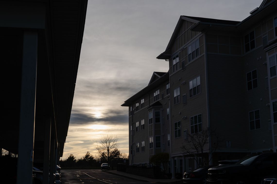 A beige apartment complex with some cars parked nearby is visible on the right of the photo, at dusk.