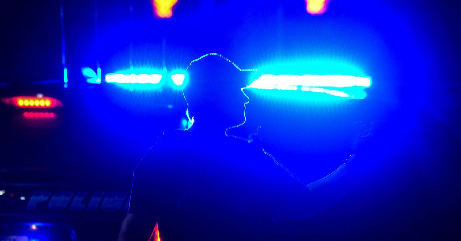 Traffic lights highlight the silhouette of a police officer as they wave their arm. 