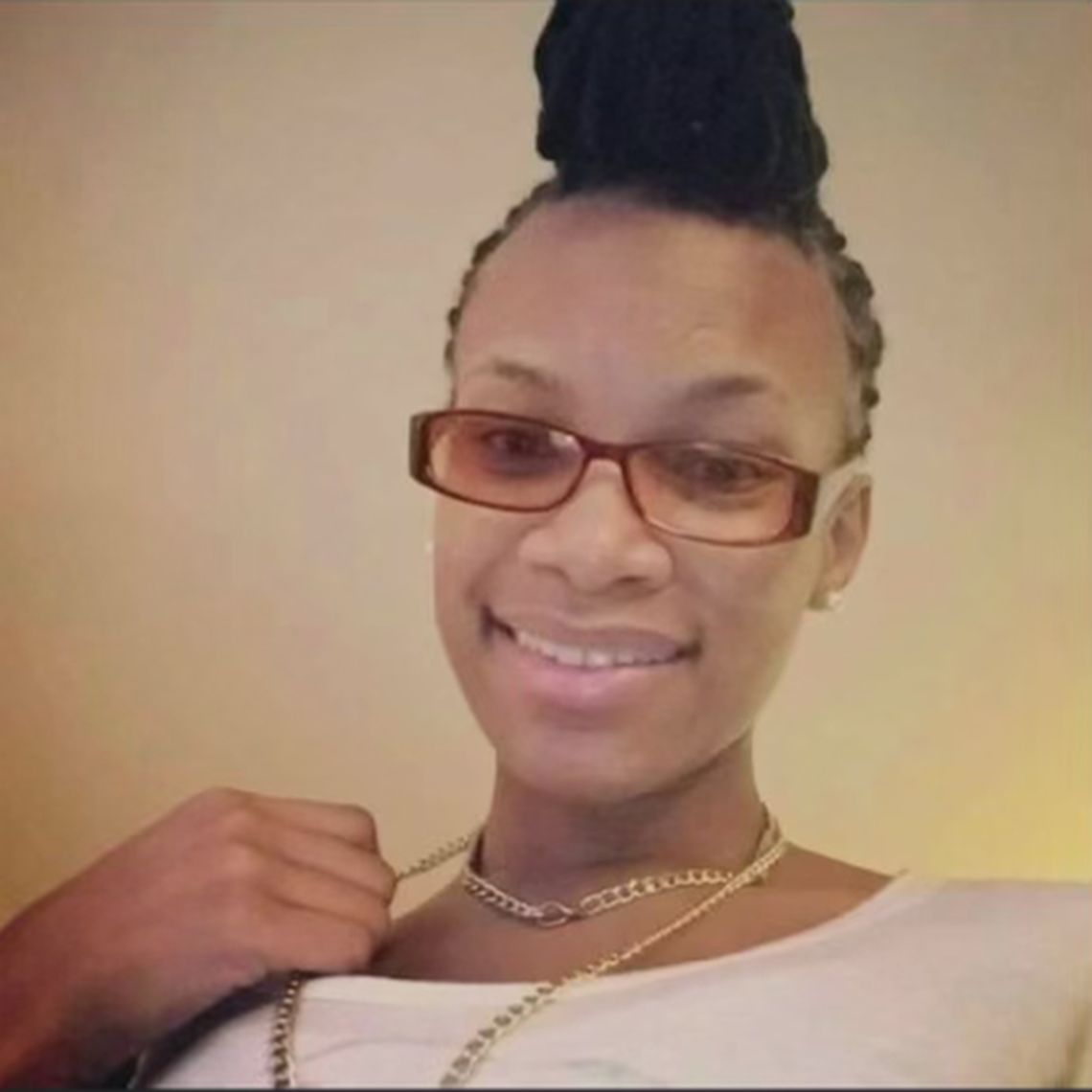 A Black woman with a high bun and glasses looks towards the camera, smiling.