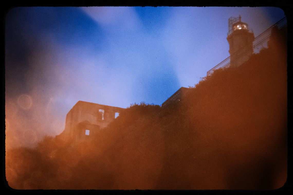 A photo shows a view of some buildings at Alcatraz with a dark blue sky above. In the light, the buildings are orange-toned. The photo has a vignette effect.