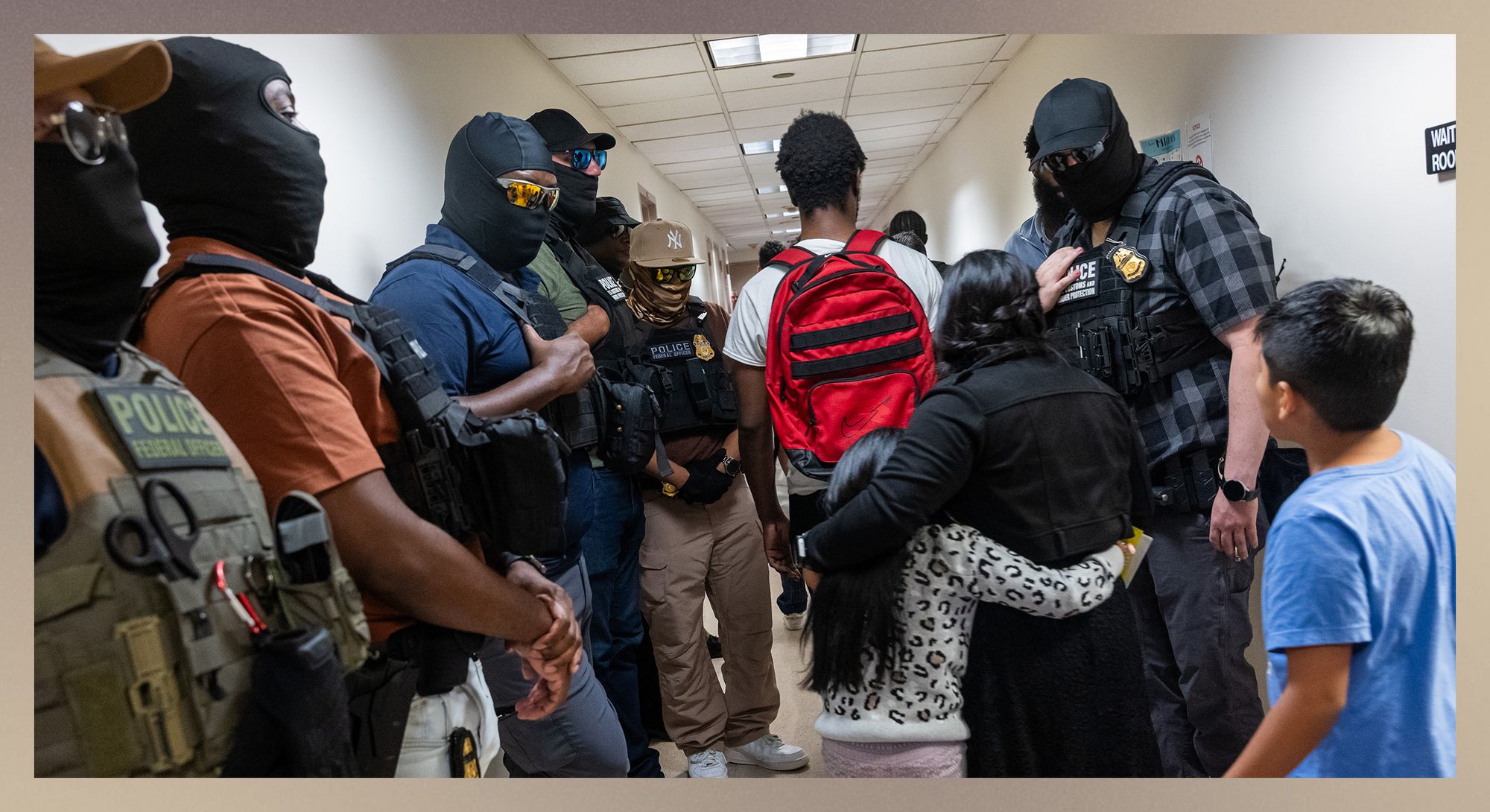 Masked federal agents, including members of ICE, stand on either side of a hallway. A person wearing a white T-shirt and red backpack walks down the center of the hallway with their back to the camera. A woman and a young child, both with dark hair, walk behind the person with their arms around each other. A young boy with dark hair and a blue T-shirt follows behind them. 