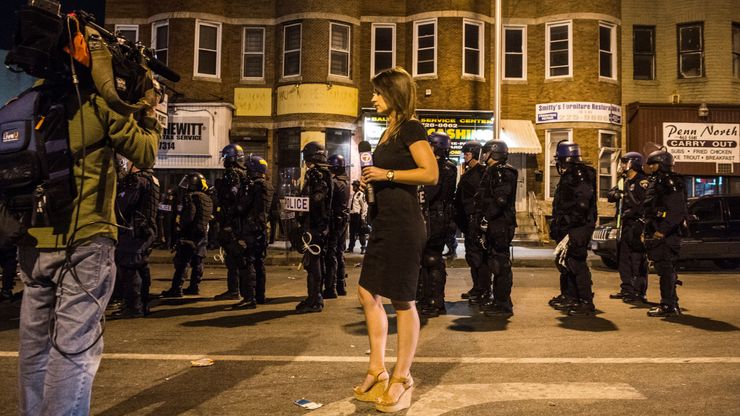 A reporter broadcasts while police give orders for crowds to disperse in West Baltimore after the 2015 funeral of Freddie Gray, who died in police custody. 