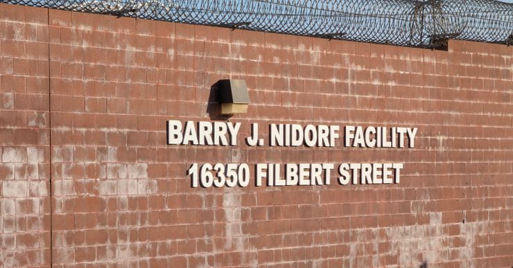 A photo shows a brick wall with barbed wire and a sign that reads, "Barry J. Nidorf Facility, 16350 Filbert Street." 