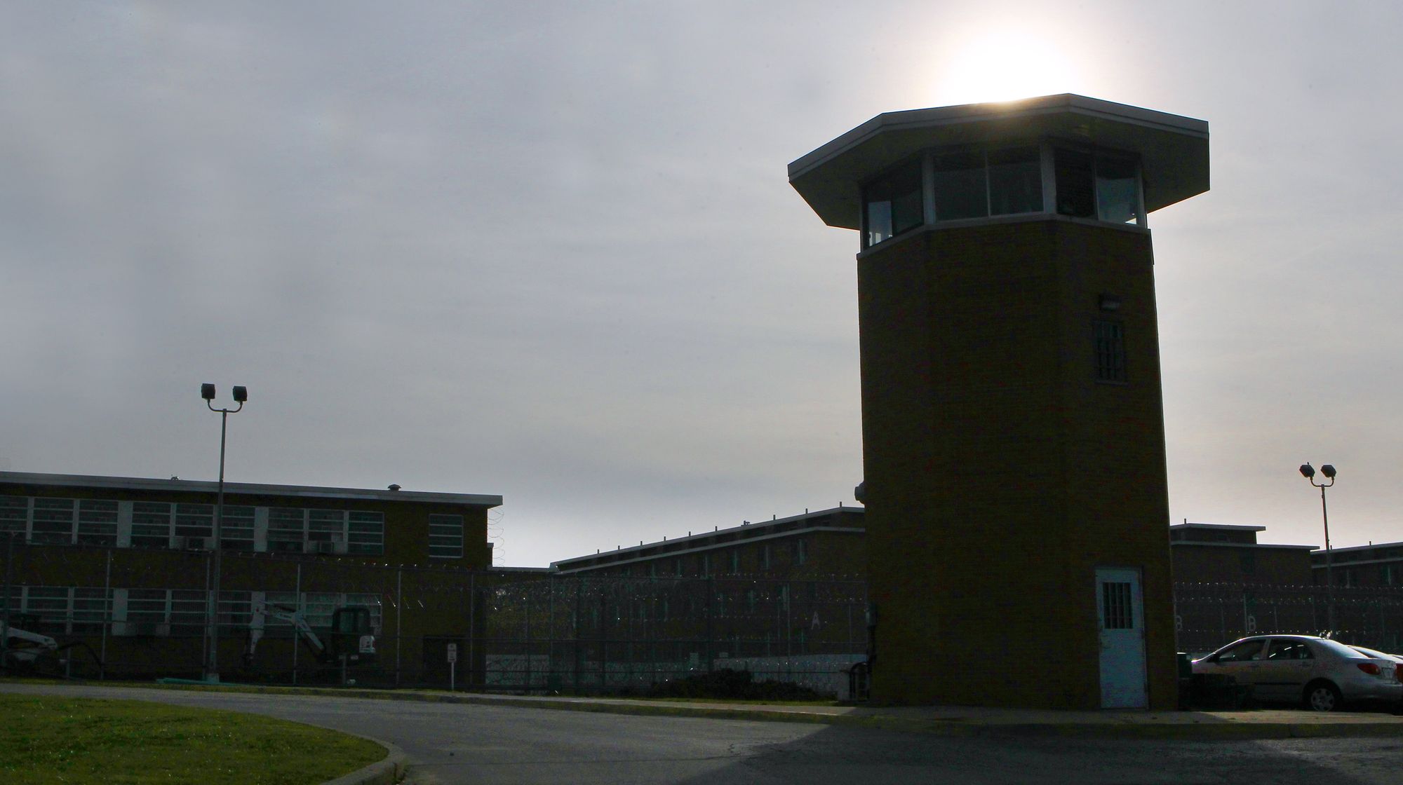 A photo shows the Lebanon Correctional Institution, which is backlit by sunlight. There is one taller guard tower and a lower building to the left. 