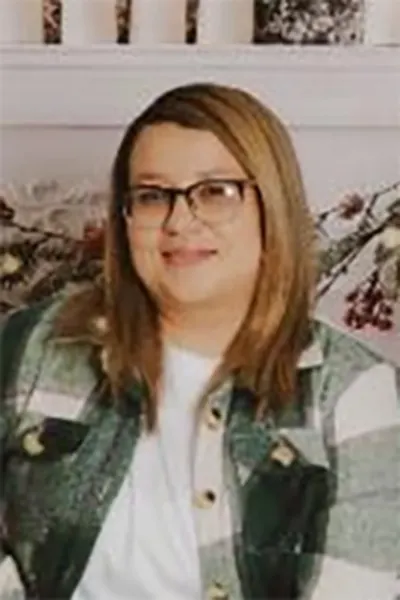 A photo shows a Latina woman, wearing glasses, a white shirt and a flannel jacket. 