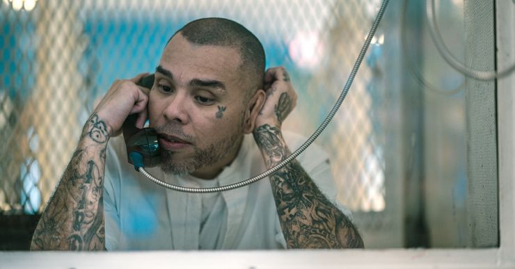 A light-skinned Hispanic man with close-cropped hair and tattoos on his arms uses the phone at the Polunsky Unit prison facility.