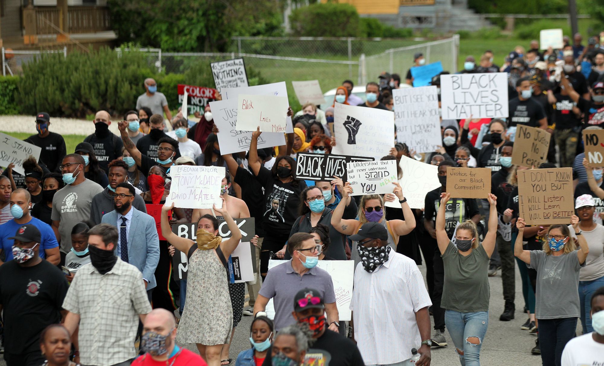 A large group of protesters march holding signs, including one that says “Black Lives Matter.”