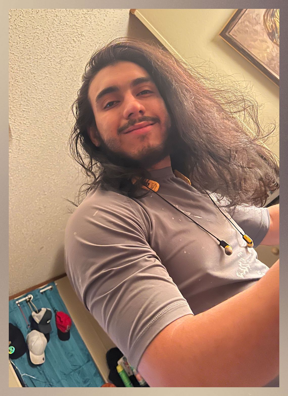 A photograph of an olive-skinned man with long brown hair and a beard smiling while looking at the camera. 