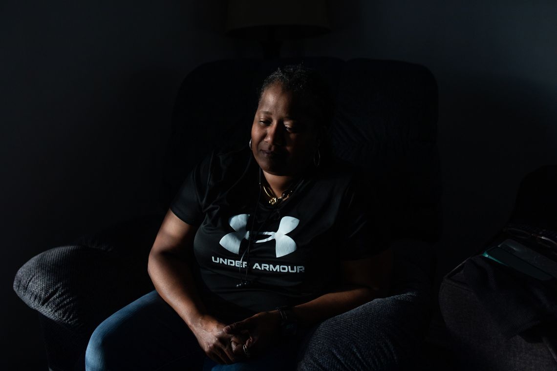 A photo shows a Black woman wearing a black T-shirt sitting on a couch looking sad. 