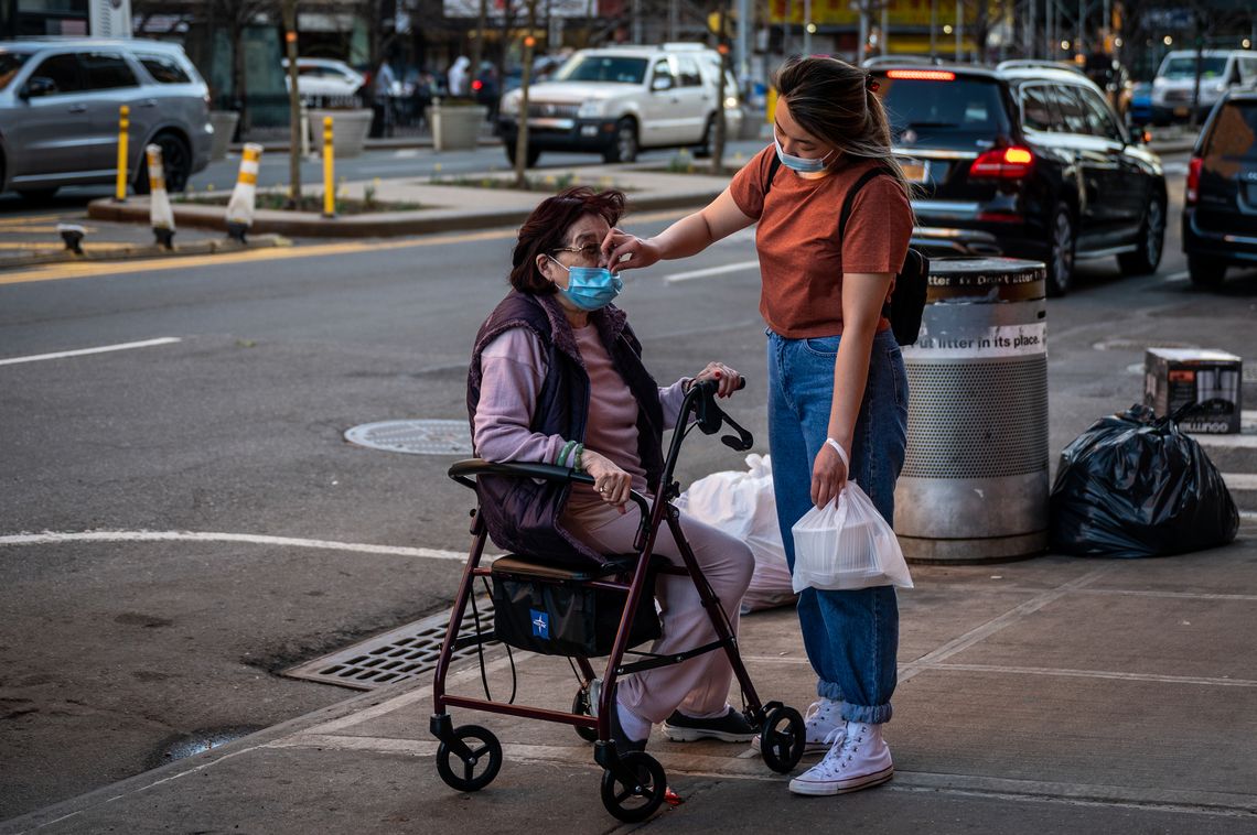 A woman lifts a face mask over an older person’s nose.