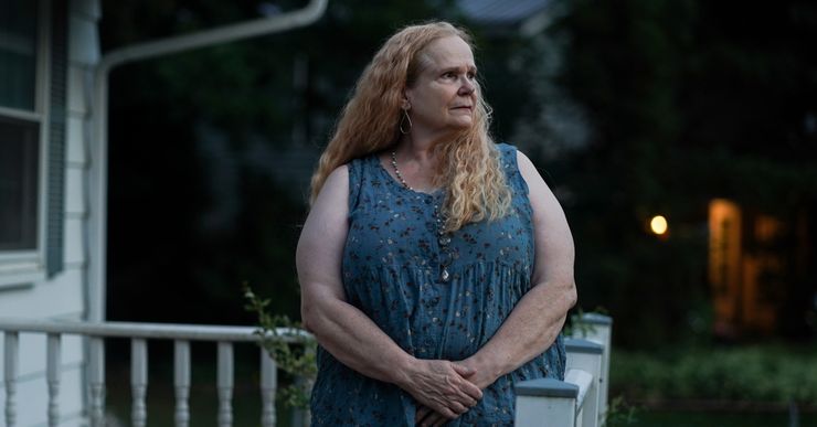 A White woman with wavy blonde hair stands on her porch at dusk.  