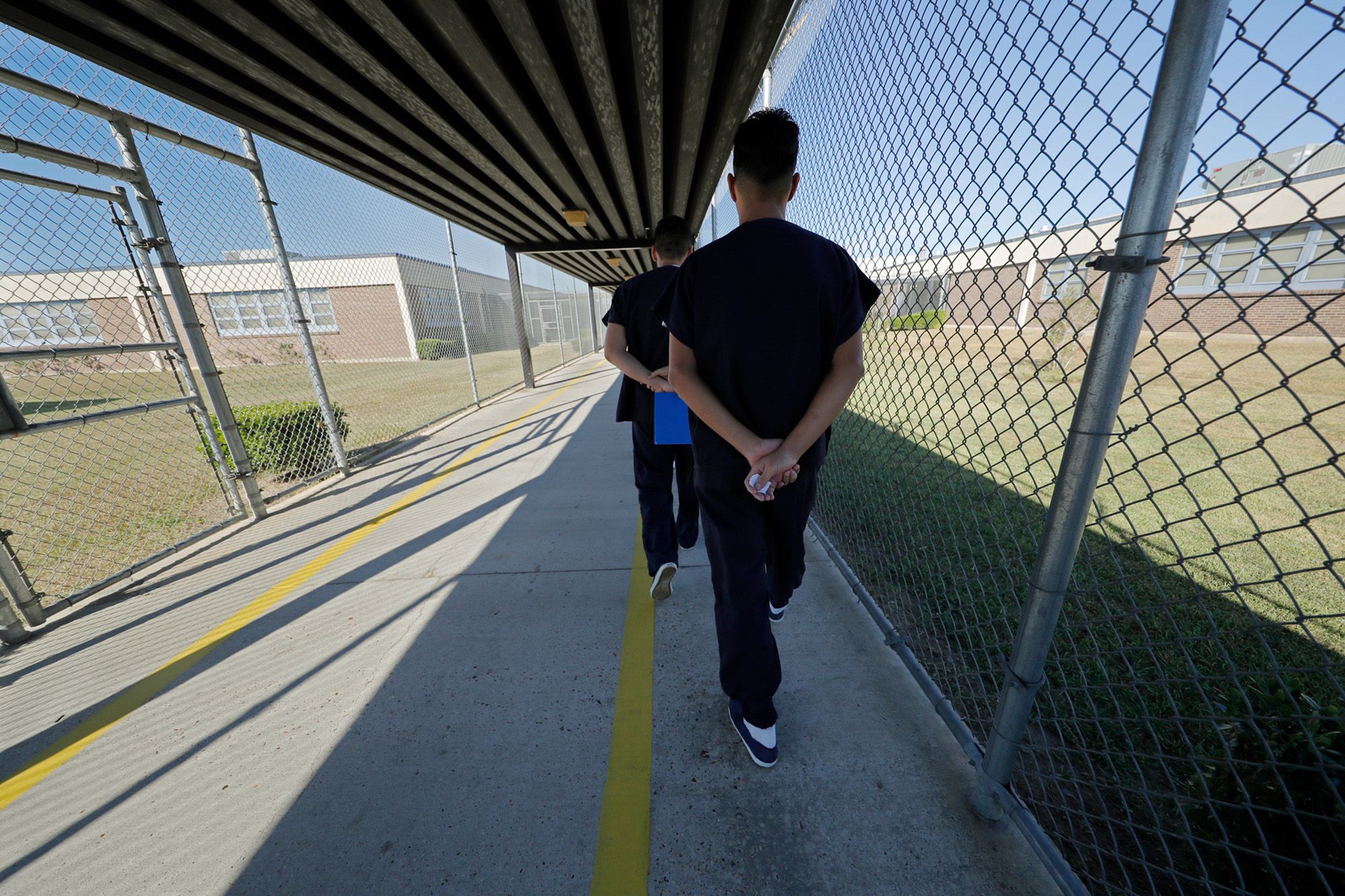 Two men wearing black uniforms clasp their hands behind they walk through a fenced pathway. 