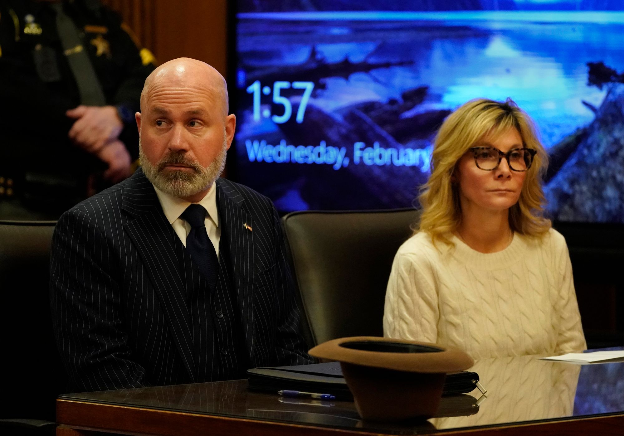 A photo shows Leslie Ann Celebrezze, right, a White woman with blonde hair and glasses, wearing an ivory sweater, sitting next to her attorney, Ian Friedman, a White man with a gray beard and wearing a black suit, in a courtroom.