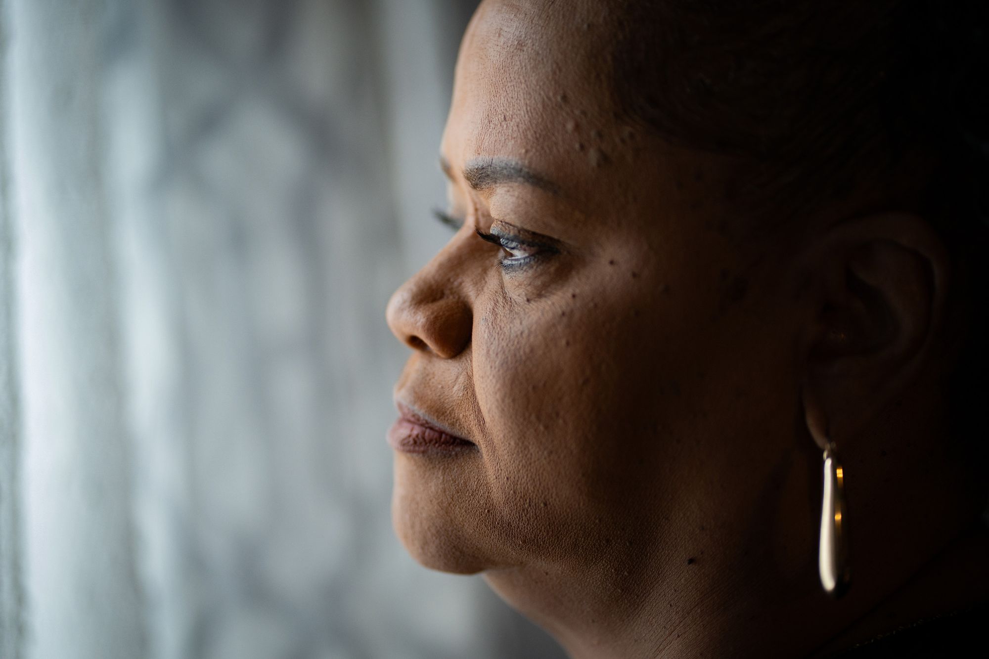 A close-up photo portrait of a Black woman looking out a window. 