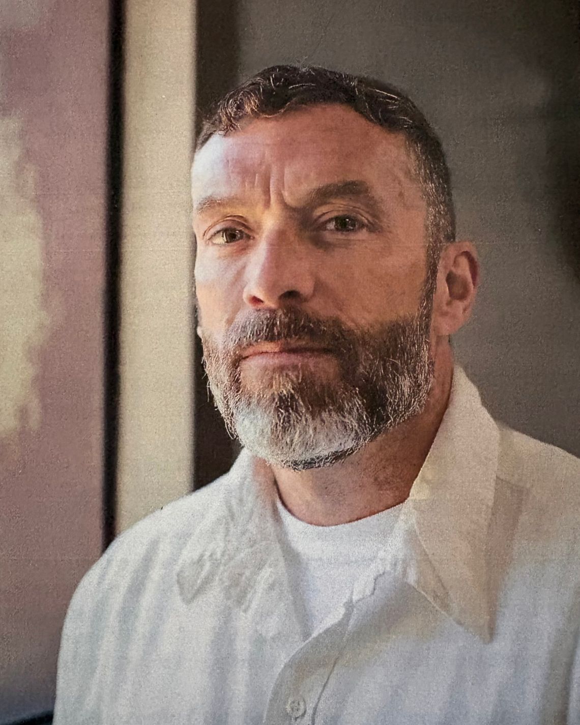 A White man, wearing a white prison uniform, poses for a portrait. 