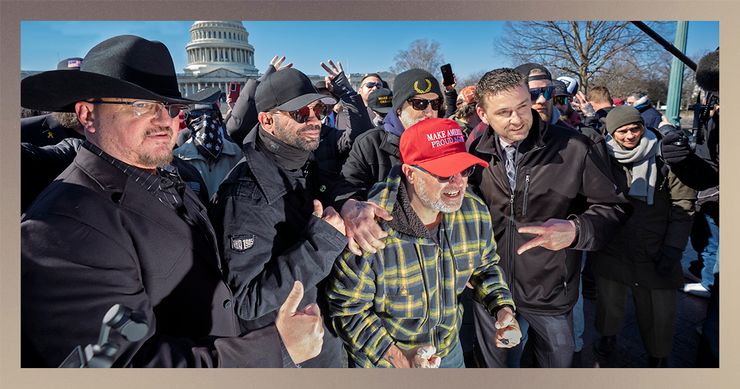 A group of men, including from left, Stewart Rhodes, a man with light-toned skin, wearing a black hat and glasses with a patch over his left eye, and Enrique Tarrio, a man with medium-toned skin, wearing sunglasses and a black baseball cap, stand outside in Washington, D.C. Both have their thumbs up. 