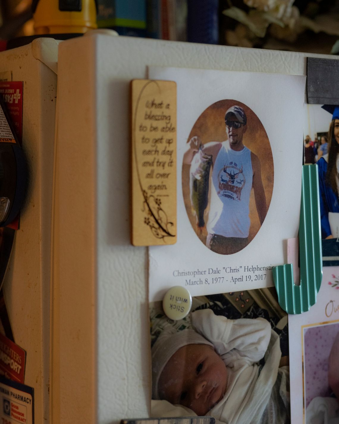 A card, showing a photo of a White man holding a fish, reads "Christopher Dale ‘Chris’ Helphenstine, March 8 1977-April 19, 2017." A photo of a baby hangs below it.