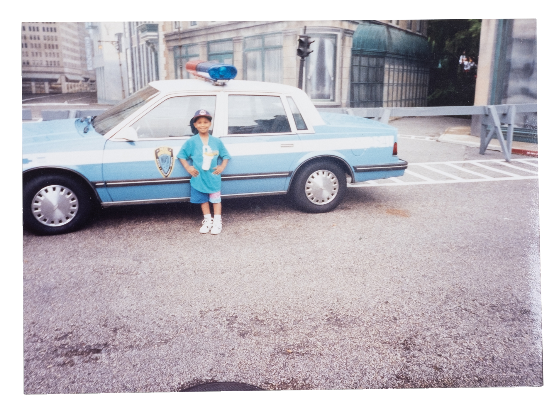 Wilbert L. Cooper as a child, wearing a blue-and-white uniform, standing in front of a blue-and-white police vehicle.