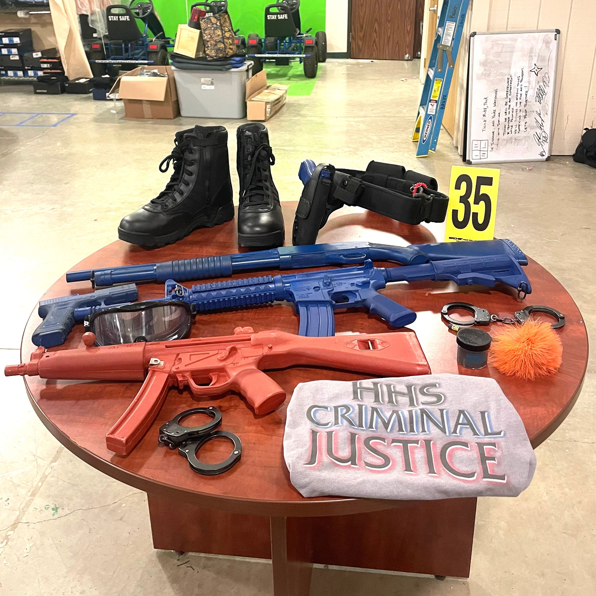 Equipment laid out on a table include uniform boots, utility belt, mock weapons, handcuffs, safety glasses and a folded shirt that reads, “HHS criminal justice.” 