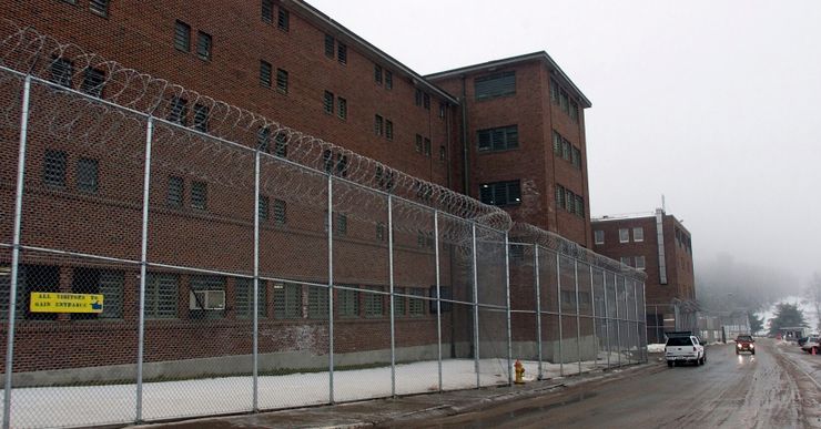 A red brick correctional facility behind a barbed wire fence. 
